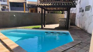 Ein Schwimmbecken mit gefliestem Deck, einer Pergola und einer kleinen Sitzgruppe im Freien.