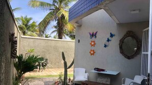 Ein Innenhof mit Steinboden, weißen Stühlen, einer hölzernen Bank und einem kleinen Tisch. An der Wand sind dekorative Schmetterlinge und Blumen angebracht.