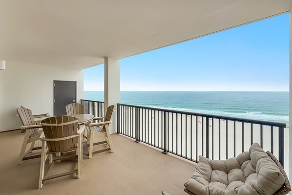 A balcony with a view of the ocean, a table with chairs, and a cushioned chair.