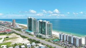 A high-rise hotel with a glass facade overlooking a beach and ocean. - RELAX AT THE  BEACH IN THIS GORGEOUS GULF FRONT CONDO! THE PALMS #914 (Orange Beach)