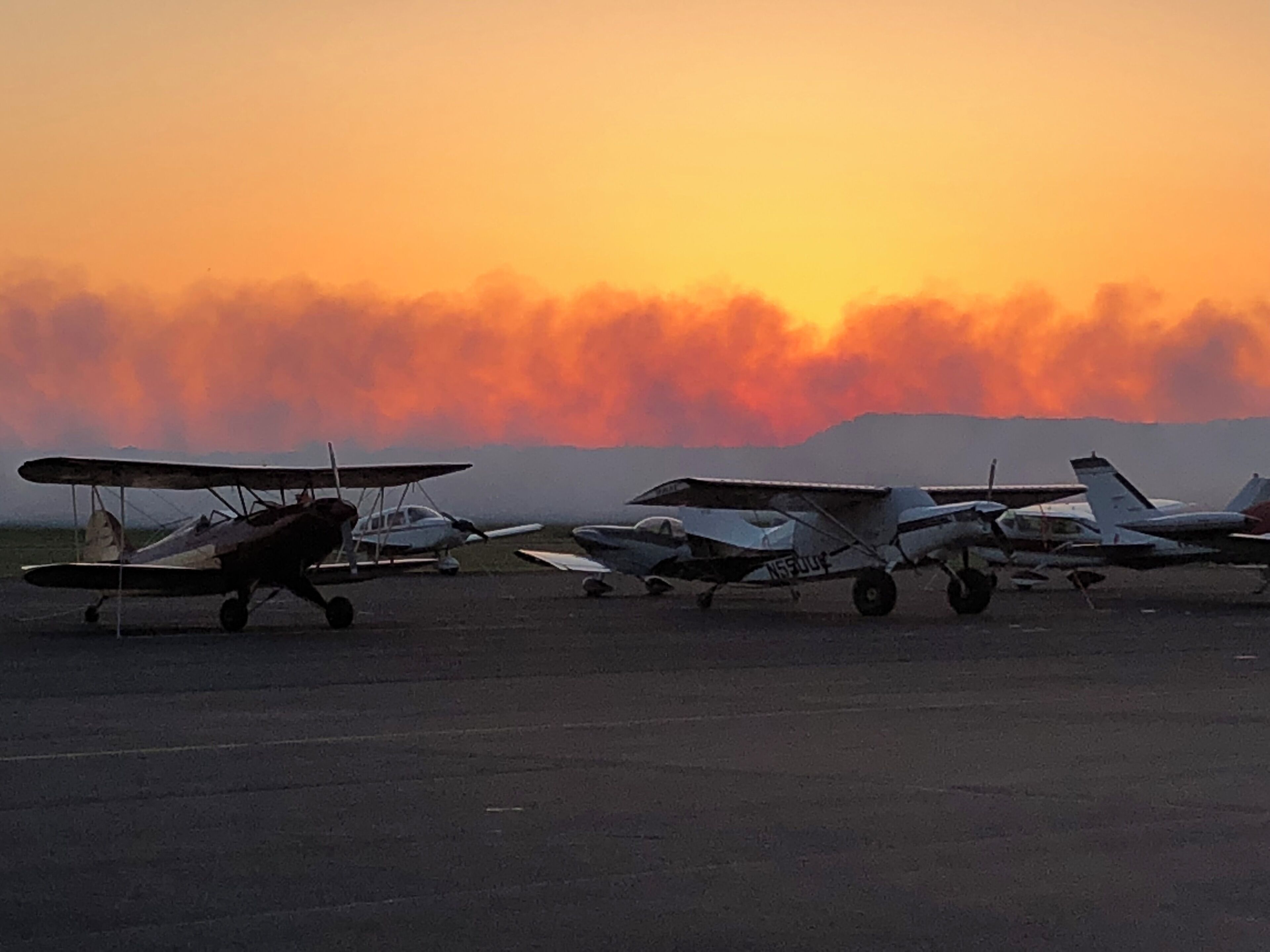 Una fila di piccoli aeromobili parcheggiati sull'asfalto al tramonto.
