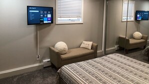 A hotel room with a bed, a sofa, a TV mounted on the wall, and a window with blinds. - Raven’s Nest - Cozy, Northern Lights, Private (North Pole)