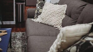A living room with a grey sofa, a patterned throw pillow, and a blue table with a placemat. - Raven’s Nest - Cozy, Northern Lights, Private (North Pole)