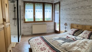 Een slaapkamer met een houten hoofdbord, een groot bed met beddengoed met een patroon, een raam met gordijnen, een radiator en een nachtkastje met een lamp.