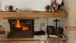Een open haard met een bakstenen omlijsting, een klein plankje erboven met decoratieve objecten, en een hand die naar de open haard wijst.