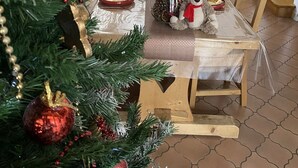 Een eethoek met een lange tafel gedekt voor een maaltijd, een kerstboom op de voorgrond en een kastje achterin.