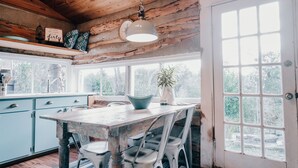 A rustic kitchen with wooden beams, a large window, and a dining table with chairs. - The Best Little Shorehouse in Texas (Volente)