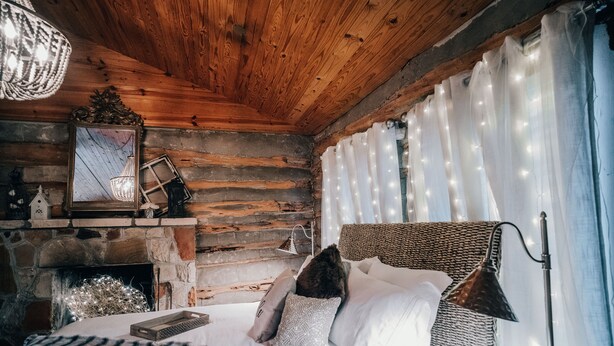 A cozy log cabin bedroom with a stone fireplace, a bed with white bedding, and a hanging light fixture. - The Best Little Shorehouse in Texas (Volente)