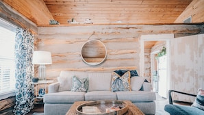A cozy log cabin interior with a sofa, a coffee table, and a hanging light fixture. - The Best Little Shorehouse in Texas (Volente)