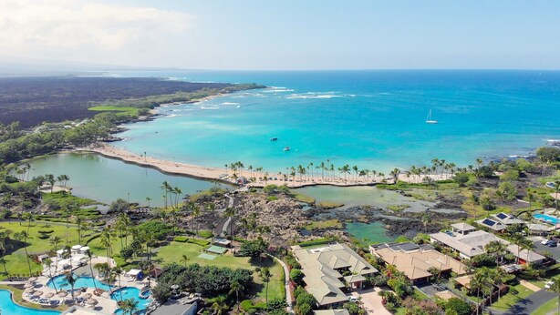 An aerial view of a coastal resort with a beach, swimming pools, and residential buildings. - Upgraded Condo on Golf Course, Walking Distance to Beach and Shops! (Waikoloa)