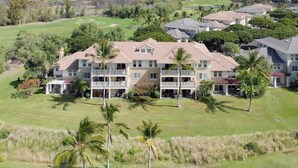 A multi-story hotel with a central courtyard, surrounded by lush greenery and palm trees. - Upgraded Condo on Golf Course, Walking Distance to Beach and Shops! (Waikoloa)