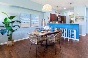 A dining area with a wooden table, wicker chairs, and a blue accent wall. - Upgraded Condo on Golf Course, Walking Distance to Beach and Shops! (Waikoloa)