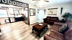 A living room with a brown leather sofa, a wooden coffee table, and a kitchen area with white cabinets and a refrigerator. - Spacious "The Lodge" 3 bed 2 bath w/Pool and plenty of Boat or RV parking!! (Mount Dora)