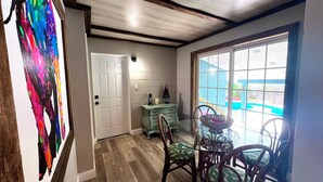 A room with a wooden floor, a white door, a teal dresser, a glass table with chairs, and a view through a large window. - Spacious "The Lodge" 3 bed 2 bath w/Pool and plenty of Boat or RV parking!! (Mount Dora)