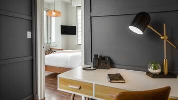 A modern hotel room with a desk, a telephone, a lamp, and a bedside table with a plant.