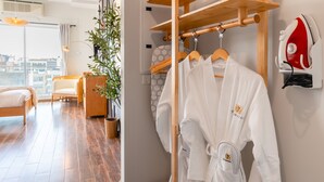 A modern hotel room with a wooden floor, a bed, a chair, a potted plant, and a wooden wardrobe with a hanging iron.