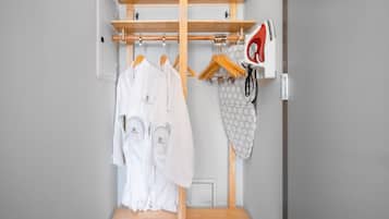 Un armario de madera con varios estantes y una barra para colgar, que contiene batas blancas y una toalla estampada.