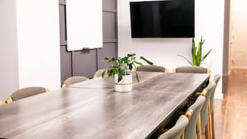 Une salle de conférence avec une longue table, des chaises, un tableau blanc, un téléviseur et une plante en pot.