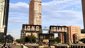 A waterfront promenade with a bridge labeled "LONG ISLAND" and modern high-rise buildings in the background.