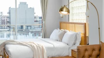 A bedroom with a large window, a bed with white bedding, a wooden headboard, and a gold floor lamp.