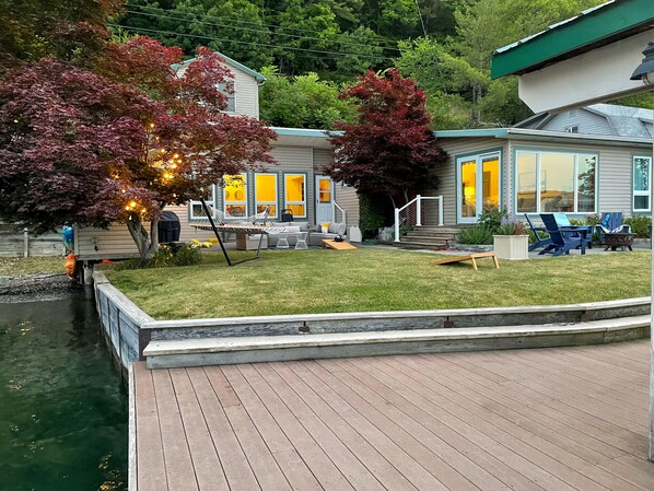 A house with a deck, a grassy yard, and a dock extending into a body of water.
