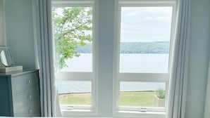 A bedroom with a large window overlooking a lake and greenery.