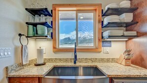 Una cocina con encimeras de granito, un lavamanos de acero inoxidable, lavavajillas y ventana con vistas a la montaña.