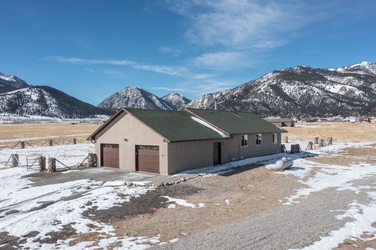 A single-story building with a green roof, a garage, and a fenced area with hay bales.