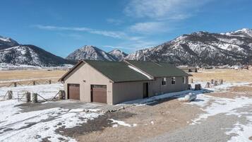 A single-story building with a green roof, a garage, and a fenced area with hay bales.