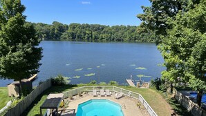 A swimming pool with a deck, surrounded by a wooden fence, and overlooking a lake with lily pads.