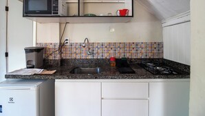 A kitchen with a microwave, sink, stove, and a tiled backsplash. - Studio Garden, cozy and unique (SC)