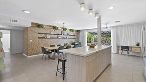 Una cocina moderna con una isla central, estantes empotrados y un comedor con sillas.