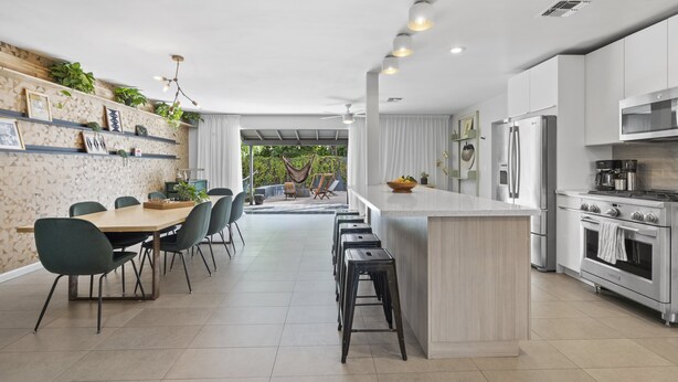 Una cocina moderna con armarios blancos, una isla central y un comedor con sillas y una mesa.