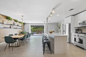 A modern kitchen with white cabinets, a central island, and a dining area with chairs and a table. - Mid-Century Stunner // Large Yard and Patio for Indoor/Outdoor Living (Phoenix)