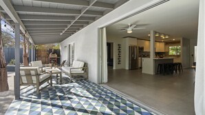 Un patio amplio con piso de baldosas geométricas, una zona de estar con sillas y vistas a una cocina moderna con taburetes de bar.