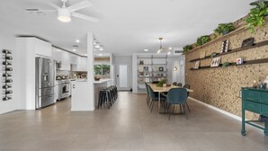 Una cocina moderna con electrodomésticos de acero inoxidable, un comedor con mesa y sillas de madera, y una pared decorativa con plantas.