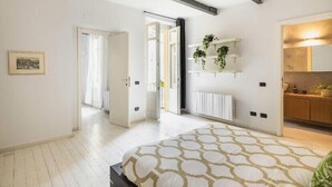 Ein Schlafzimmer mit einem Bett, einem Heizkörper, einer Pflanze und einer Tür zu einem anderen Raum.