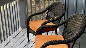 Two wicker chairs with orange cushions on a wooden deck with a gray railing.