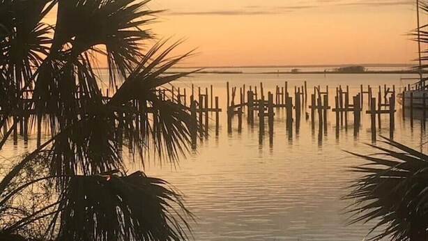 A calm waterfront scene with a sunset, palm trees, and wooden docks.