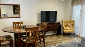 A living room with a dining table, chairs, a sofa, a TV, a ceiling fan, and a patterned rug.