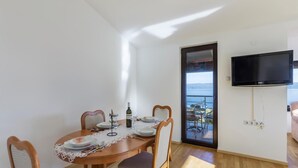 A dining area with a round table, chairs, and a television mounted on the wall. - Nice apartment in Labin with house sea view (Labin)