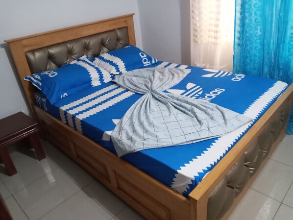 A bed with a blue and white Adidas-themed bedspread, a grey blanket, and a wooden headboard.