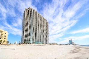 Ein Hochhaus-Hotel mit mehreren Etagen und Balkonen, direkt an einem Sandstrand gelegen, mit blauem Himmel.