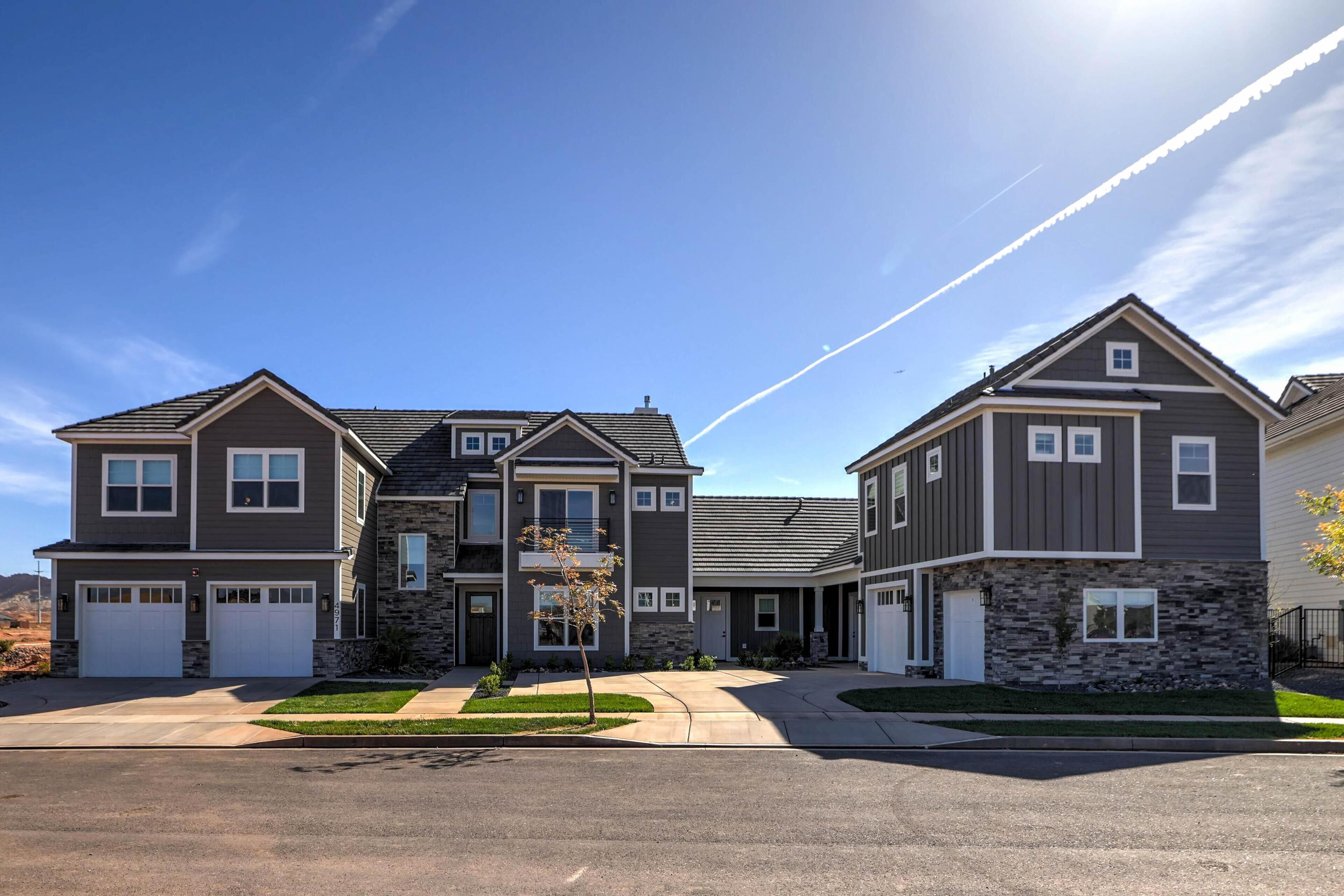 A modern two-story residential building with a stone facade, a central entrance, and a driveway leading to a garage.