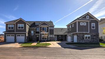 A modern two-story residential building with a stone facade, a central entrance, and a driveway leading to a garage.