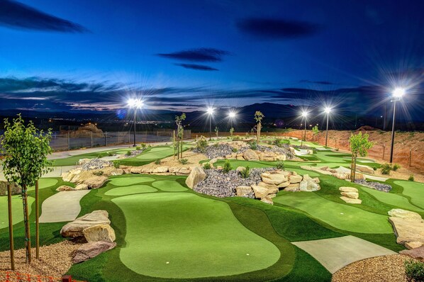 A golf course at night with well-lit areas, green fairways, and bunkers.