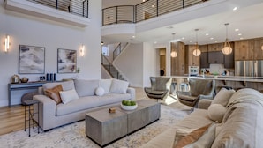 A spacious living area with a high ceiling, a modern kitchen, and a staircase connecting the floors. - New | Family Reunions | Corporate Retreats | Private Pool |  Sleeps 23 (Washington)