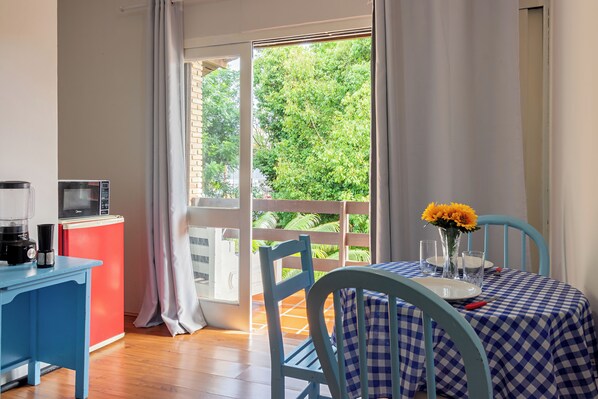 A room with a table set for two, a coffee maker, a microwave, and a view of greenery outside.