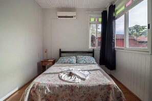 A bedroom with a bed, a nightstand, a window with curtains, and an air conditioning unit.