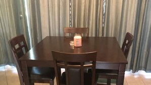 A dining table with four chairs, a candle, and a curtain in the background. - 1085 Cozy 1 Bedroom Condo on Mobile Bay (Daphne)